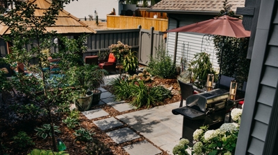 A backyard patio with pavers, plants, a gazebo, a grill, and patio furniture. Photo